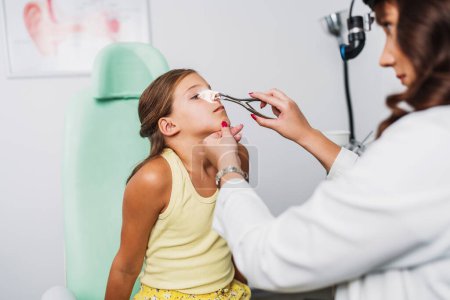 Female audiologist examining girl ear using otoscope in doctors office. Child receiving a ear exam. Nose and throat medical examination. Healthcare and medicine concept. 