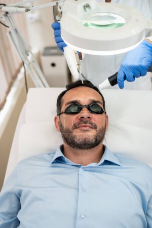 Photo for Handsome middle age bearded man receiving modern face lifting treatment. Gama laser face lifting, acne and scar removal. Modern medical non-surgical ultrasound skin lift treatment. - Royalty Free Image