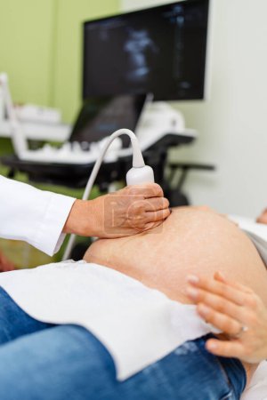 Téléchargez les photos : Médecin femme faisant une échographie pour une belle femme enceinte. Vue latérale. Concept moderne de grossesse et de soins de santé. - en image libre de droit