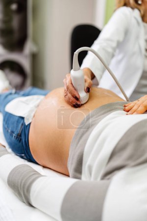 Téléchargez les photos : Médecin femme faisant une échographie pour une belle femme enceinte. Vue latérale. Concept moderne de grossesse et de soins de santé. - en image libre de droit