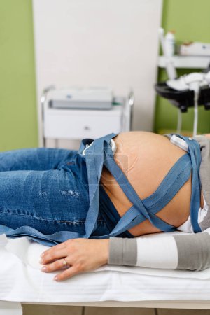 Téléchargez les photos : Beautiful young pregnant woman at electrocardiograph check up for baby health and expected date of birth. Fetal heart monitoring. Healthcare and medical service concept. - en image libre de droit
