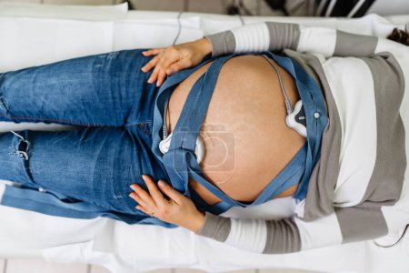 Téléchargez les photos : Belle jeune femme enceinte à l'électrocardiographe vérifier la santé du bébé et la date de naissance prévue. Surveillance cardiaque du fœtus. Concept de soins de santé et de services médicaux. - en image libre de droit