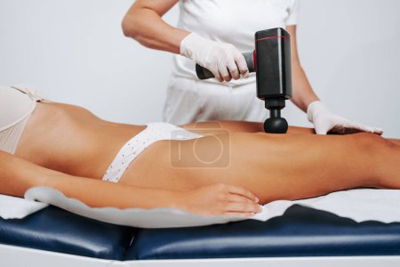 Photo for Young sporty caucasian woman having body massage using percussion pistol at beauty relax center. Electric massager pistol for special muscle treatment. Sports and pain recovery concept. - Royalty Free Image