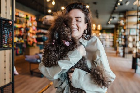 Photo for Beautiful and happy young woman sitting in modern pet shop cafe bar and enjoying in fresh coffee together with her adorable brown toy poodle. - Royalty Free Image
