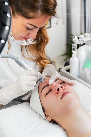 Photo for Young woman receiving hydra facial treatment for exfoliation, rejuvenation and hydration of her face skin. Modern facial hydro microdermabrasion peeling beauty procedure. Hydra vacuum cleaner. - Royalty Free Image