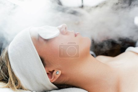 Téléchargez les photos : Jeune femme recevant un traitement de beauté avec vapeur faciale à l'ozone thermique. Cosmétologie professionnelle salon ou procédure spa. - en image libre de droit