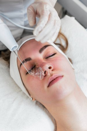 Photo for Young woman receiving face lift treatment with high-frequency wand. This modern treatment uses electric currents to kill acne-causing bacteria, reduce inflammation, and improve skin tone and texture. - Royalty Free Image