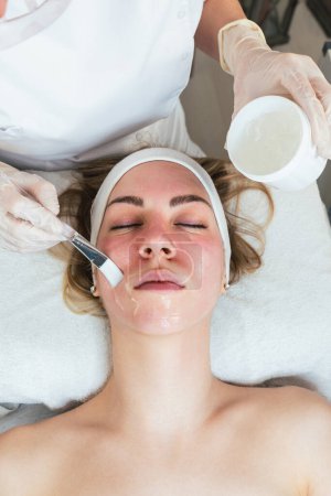 Photo for Young woman receiving modern facial low-voltage electrical treatment. Professional cosmetician putting facial gel mask on her skin during preparation procedure. Modern and popular face lifting. - Royalty Free Image