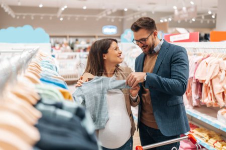 Téléchargez les photos : Attractive middle age couple enjoying in buying clothes and appliances for their new baby. Heterosexual couple in baby shop or store. Expecting baby concept. - en image libre de droit