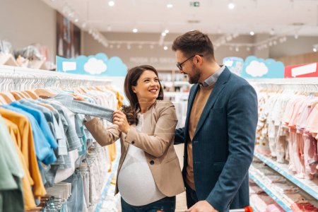 Photo for Attractive middle age couple enjoying in buying clothes and appliances for their new baby. Heterosexual couple in baby shop or store. Expecting baby concept. - Royalty Free Image