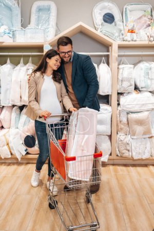 Foto de Attractive middle age couple enjoying in buying clothes and appliances for their new baby. Heterosexual couple in baby shop or store. Expecting baby concept. - Imagen libre de derechos