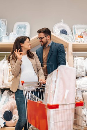 Photo for Attractive middle age couple enjoying in buying clothes and appliances for their new baby. Heterosexual couple in baby shop or store. Expecting baby concept. - Royalty Free Image