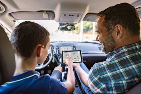 Photo for Driving instructor sitting in a car with his student and explain to him driving basics and traffic rules. He is using electronic tablet for education purpose. View from inside. - Royalty Free Image