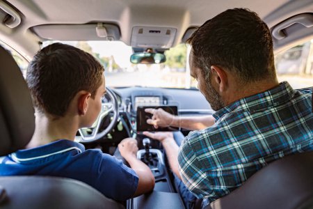 Photo for Driving instructor sitting in a car with his student and explain to him driving basics and traffic rules. He is using electronic tablet for education purpose. View from inside. - Royalty Free Image