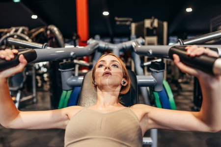 Téléchargez les photos : Belle femme rousse maigre faisant de l'exercice dans une salle de fitness spacieuse et moderne équipée. Les gens et le concept de loisirs. - en image libre de droit