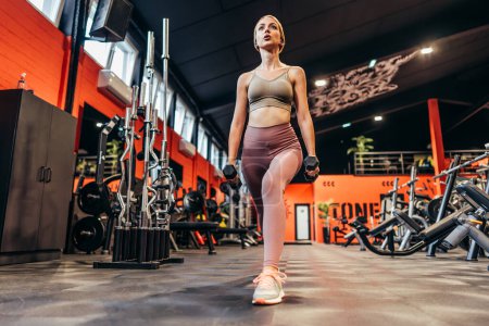 Photo for Beautiful skinny redhead woman exercising in a spacious and modern equipped fitness gym. People and recreation concept. - Royalty Free Image