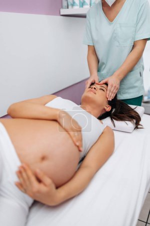 Foto de Beautiful young pregnant woman enjoying and relaxing during special massage treatment for maintaining healthy pregnancy. - Imagen libre de derechos