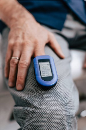 Experienced female doctor examining an male elderly patient and measures his blood oxygen saturation with a fingertip pulse oximeter or monitor. Close up shot of medical device on human finger.