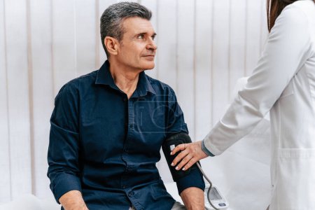 Foto de Doctora con experiencia examinando a un paciente anciano masculino y midiendo su presión arterial con esfigmomanómetro o monitor de presión arterial. - Imagen libre de derechos