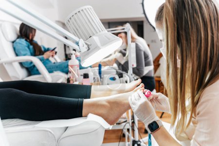 Photo for Group of professional podiatrists working in a modern nail beauty studio or spa. Satisfied clients relaxing and enjoying in a great foot and toenails treatment. - Royalty Free Image