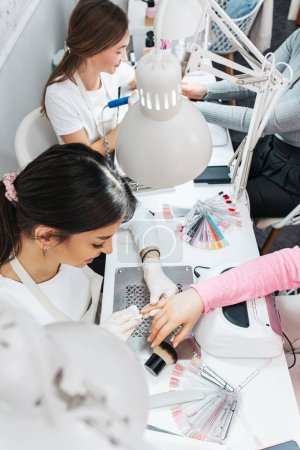 Photo for Professional manicurists working in a modern beauty salon. Satisfied female clients receiving nail manicure treatments at spa center. - Royalty Free Image