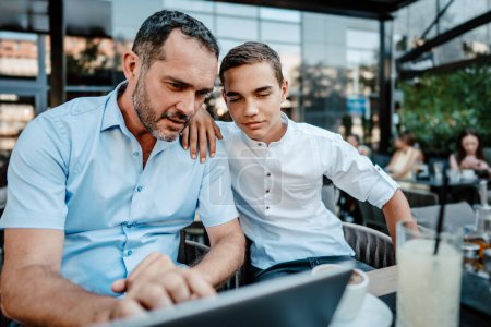 Téléchargez les photos : Beau et heureux père et son fils adolescent assis dans un restaurant et parlant. - en image libre de droit