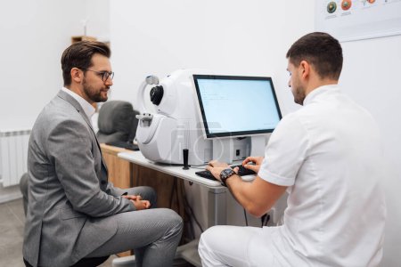 Photo for Attractive male doctor ophthalmologist is checking the eye vision of handsome middle age man in modern clinic. Doctor and patient during medical check up in ophthalmology clinic. - Royalty Free Image