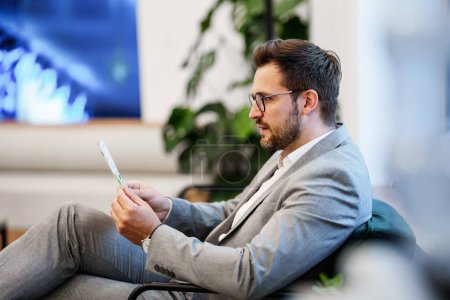 Photo for Handsome man sitting and waiting for a eyesight checkup in a modern clinic for diagnosis and treatment of eye and sight diseases. He has difficulty reading due to illness or visual impairment. - Royalty Free Image