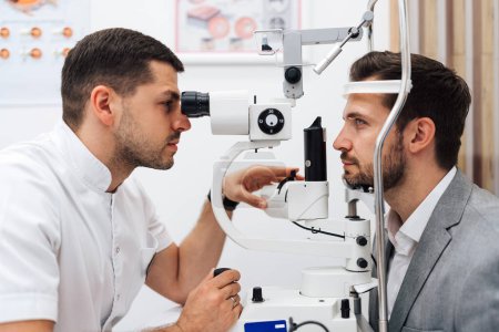 Photo for Attractive male doctor ophthalmologist is checking the eye vision of handsome middle age man in modern clinic. Doctor and patient during medical check up in ophthalmology clinic. - Royalty Free Image