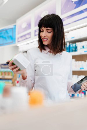 Téléchargez les photos : Magnifique pharmacien travaillant et se tenant dans une pharmacie et faisant un bilan. Portrait d'un travailleur de la santé positif ou d'un chimiste à son travail. - en image libre de droit