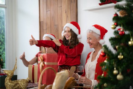 Téléchargez les photos : Famille joyeuse avec chapeaux de Père Noël s'amuser ensemble pendant Noël, donnant pouces vers le haut - en image libre de droit