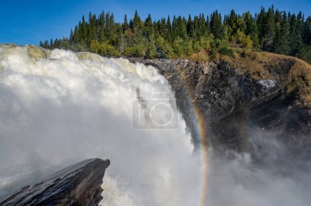 Téléchargez les photos : Célèbre cascade Tannforsen dans le nord de la Suède, avec un arc-en-ciel dans la brume et des cascades d'eau rapides. - en image libre de droit