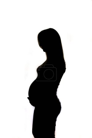 Téléchargez les photos : Beautyfull silhouette de cheveux longs femme enceinte sur un fond blanc entoureet par l'ombre. - en image libre de droit
