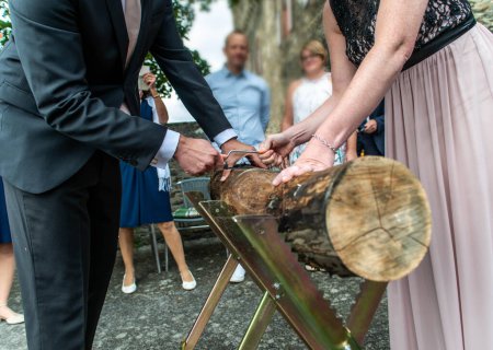 Foto de Joven pareja nupcial novio novia aserrando un tronco de árbol juntos boda alemana tradición. - Imagen libre de derechos