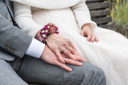 Téléchargez les photos : Mariée tenant la main du marié avec des alliances assis sur le banc. - en image libre de droit