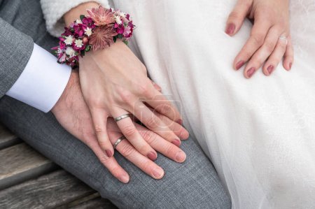 Téléchargez les photos : Mariée tenant la main du marié avec des alliances assis sur le banc. - en image libre de droit