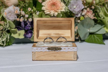 Foto de Anillo de boda almohada arpillera en caja de madera en frente de anillos de ramo de flores de amor. - Imagen libre de derechos