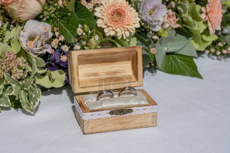 Téléchargez les photos : Bague de mariage oreiller toile de jute dans une boîte en bois devant des anneaux de bouquet de fleurs d'amour. - en image libre de droit