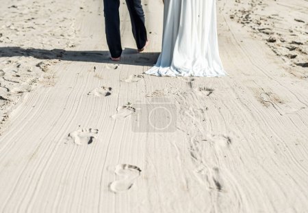 Photo for Newlyweds walking along the beach, with bride and groom dressed up for wedding. - Royalty Free Image