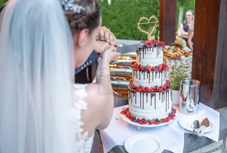 Téléchargez les photos : Mariage marié et marié Couper le délicieux gâteau de mariage fruité ensemble fruits colorés. - en image libre de droit
