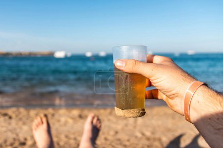Photo for Hand hold a Beer toast in the sand on Vacation in Egypt Hurghada Makadi Bay. - Royalty Free Image
