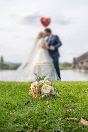 Photo for Wedding bouquet on foreground of a blurred kissing couple. Flowers and lovers. - Royalty Free Image
