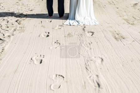 Foto de Recién casados caminando por la playa, con novia y novio vestidos para la boda. - Imagen libre de derechos