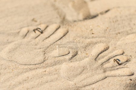 Foto de Impresiones de dos manos con anillos de boda en la playa de arena tropical, concepto de boda de playa al aire libre. - Imagen libre de derechos