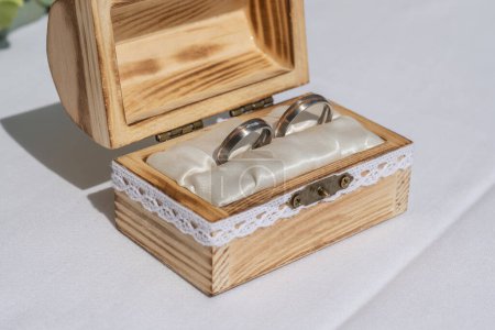 Téléchargez les photos : Bague de mariage oreiller toile de jute dans une boîte en bois devant des anneaux de bouquet de fleurs d'amour. - en image libre de droit