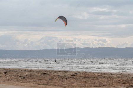 Photo for Melbystrand Sweden A kitesurfer practise his surfing skills close to beach with sand dunes. - Royalty Free Image