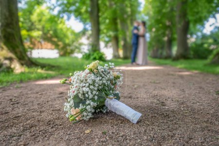 Photo for Wedding bouquet on foreground of a blurred kissing couple. Flowers and lovers. - Royalty Free Image