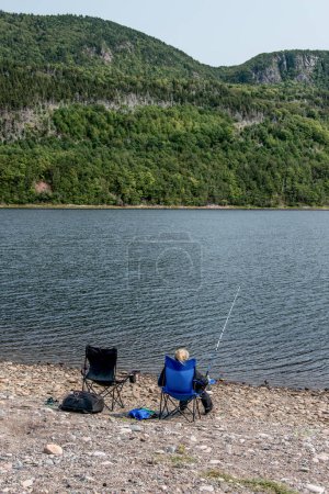 Foto de Chica pescando en el lago cerca de la línea de costa de Cabo Bretón acantilado pintoresco ruta Cabot Trail, Nueva Escocia Hghlands Canadá. - Imagen libre de derechos