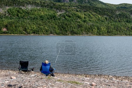 Foto de Chica pescando en el lago cerca de la línea de costa de Cabo Bretón acantilado pintoresco ruta Cabot Trail, Nueva Escocia Hghlands Canadá. - Imagen libre de derechos