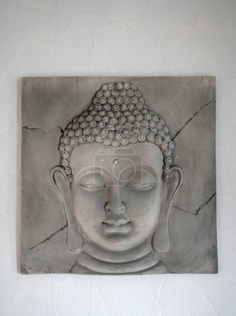 Téléchargez les photos : Photo rapprochée de la tête d'une petite statue de Bouddha en pierre accrochée à un mur blanc. - en image libre de droit